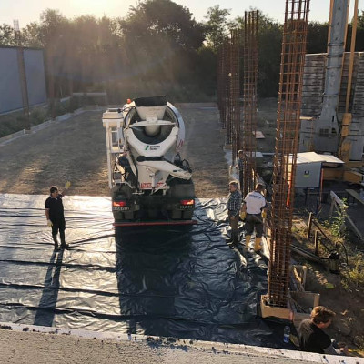Ein Betonmischerfahrzeug steht auf einer Baustelle, umgeben von Menschen und Baugerüsten.